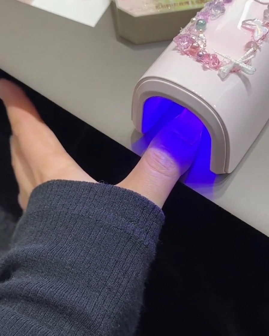 Un ongle en train de catalyser sous une lampe UV/LED rose.