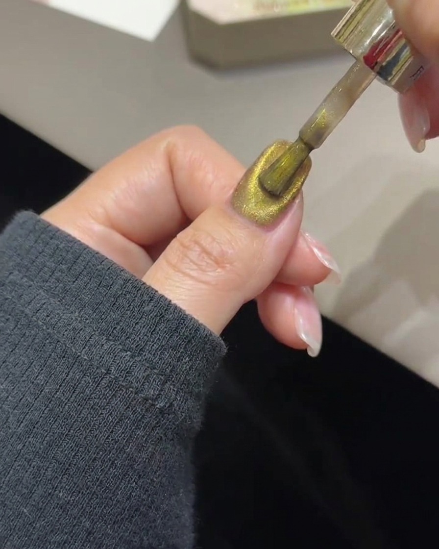 Un outil de baguette magnétique planant au-dessus dun ongle pour concentrer les particules magnétiques dorées en une bande lumineuse.