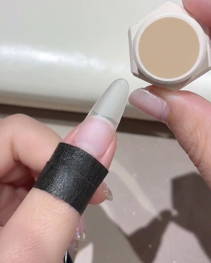 Une petite éponge appliquant une couleur de gel nude sur une extension dongle artificielle transparente.