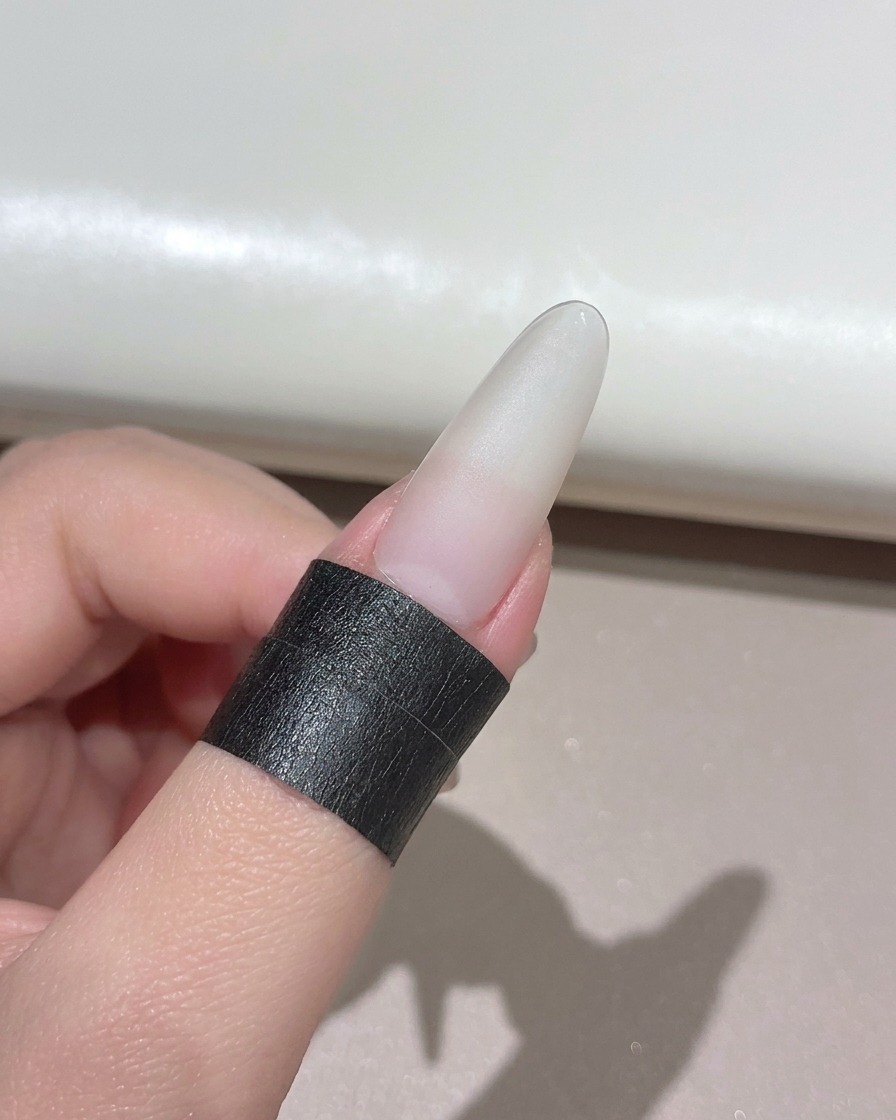 Un ongle manucuré positionné sous une lampe UV LED portable compacte.