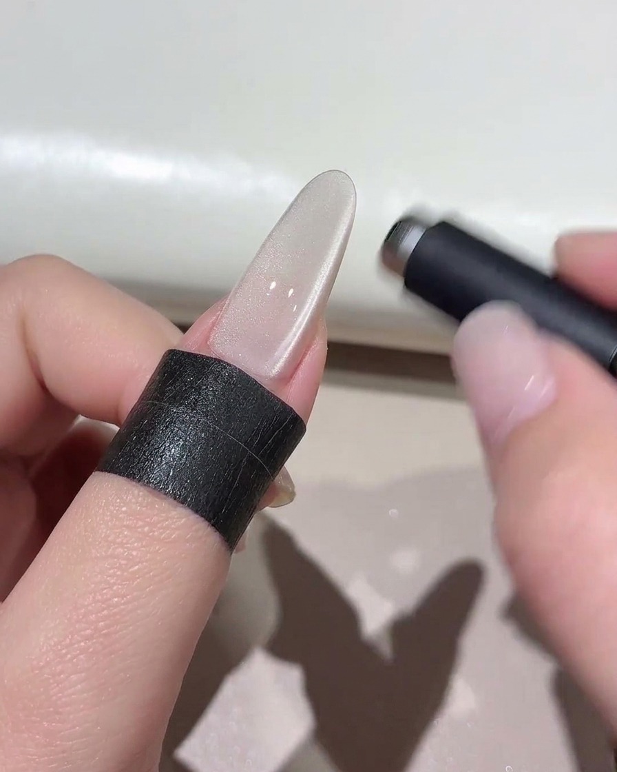 Un aimant cylindrique survolant un ongle cat-eye scintillant pour façonner leffet lumineux.