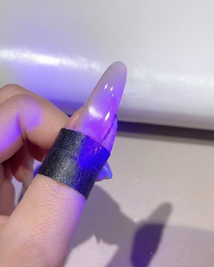 Un ongle sous une lampe UV LED violette catalysant la couche de gel cat-eye finie.