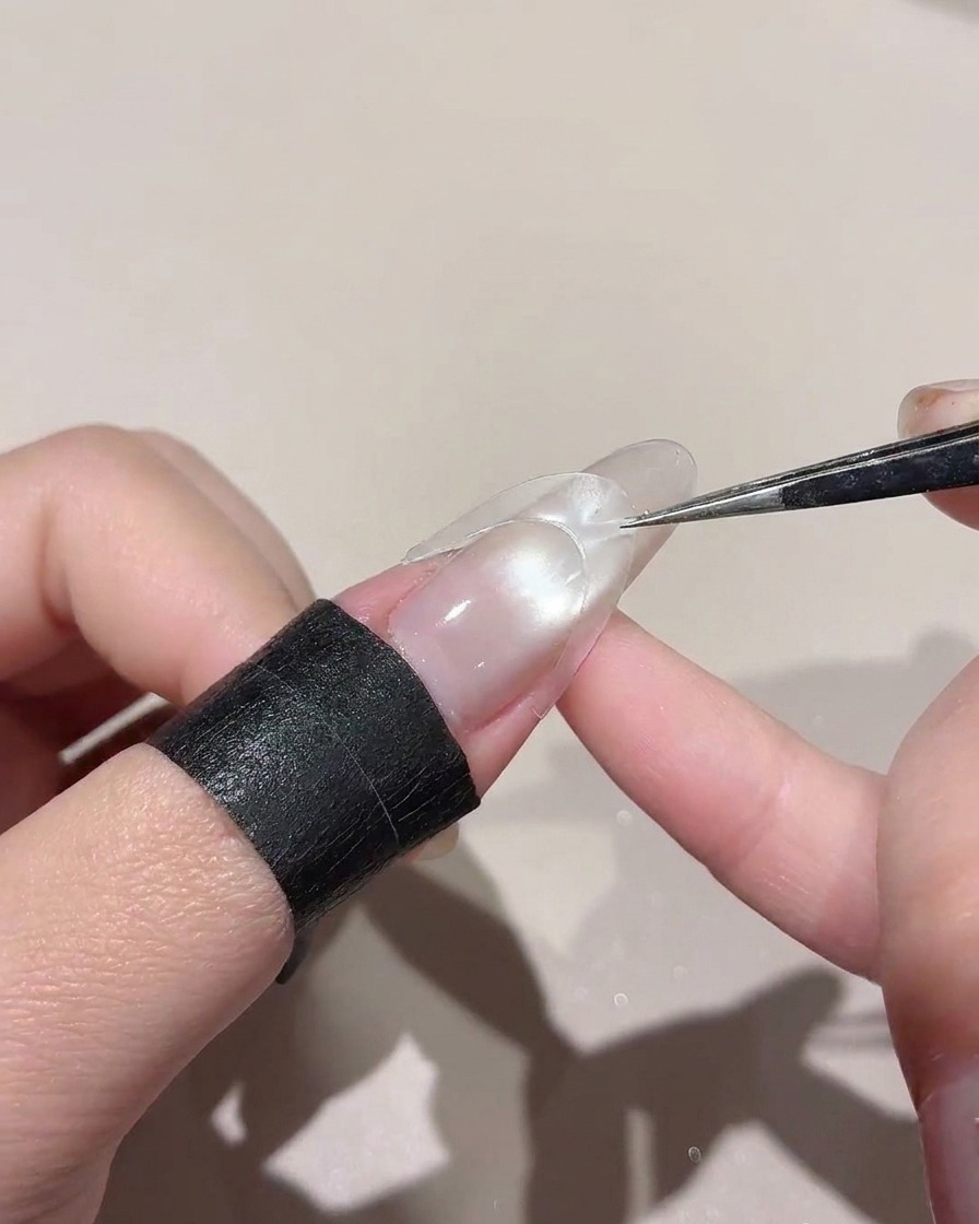 Un autocollant incurvé placé au milieu dun ongle brillant à laide de pinces.