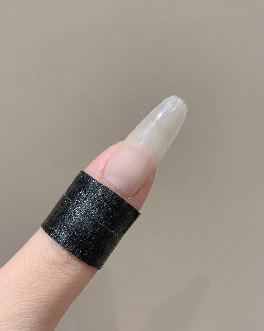 Un outil en silicone appuyant sur le bord incurvé dun autocollant pour ongle French sur un doigt.