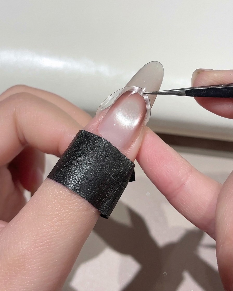 Des pinces plaçant un autocollant French incurvé légèrement plus haut sur un ongle manucuré.