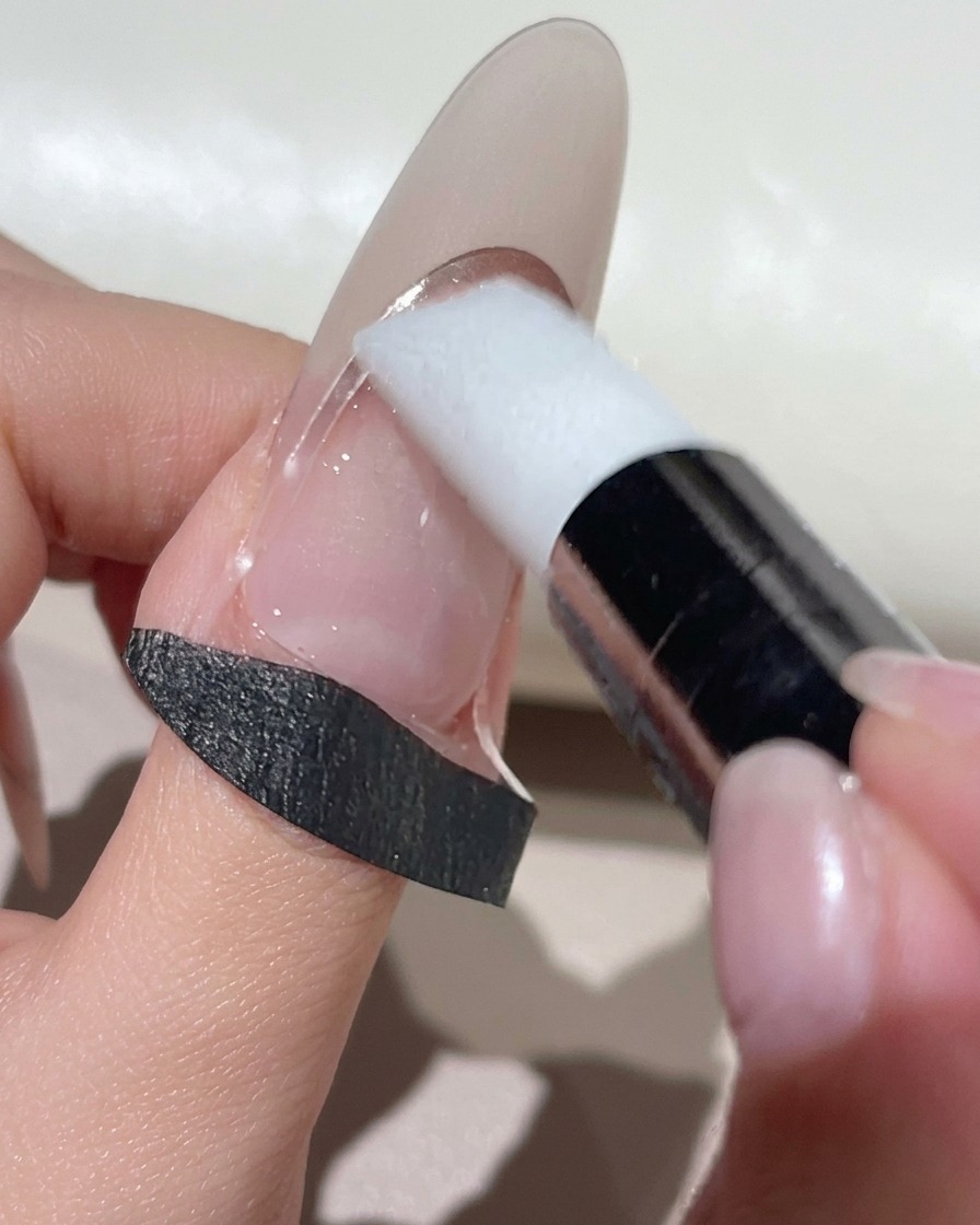 Un outil de maquillage en silicone blanc appuyant sur un autocollant guide French incurvé sur un ongle au ton naturel.
