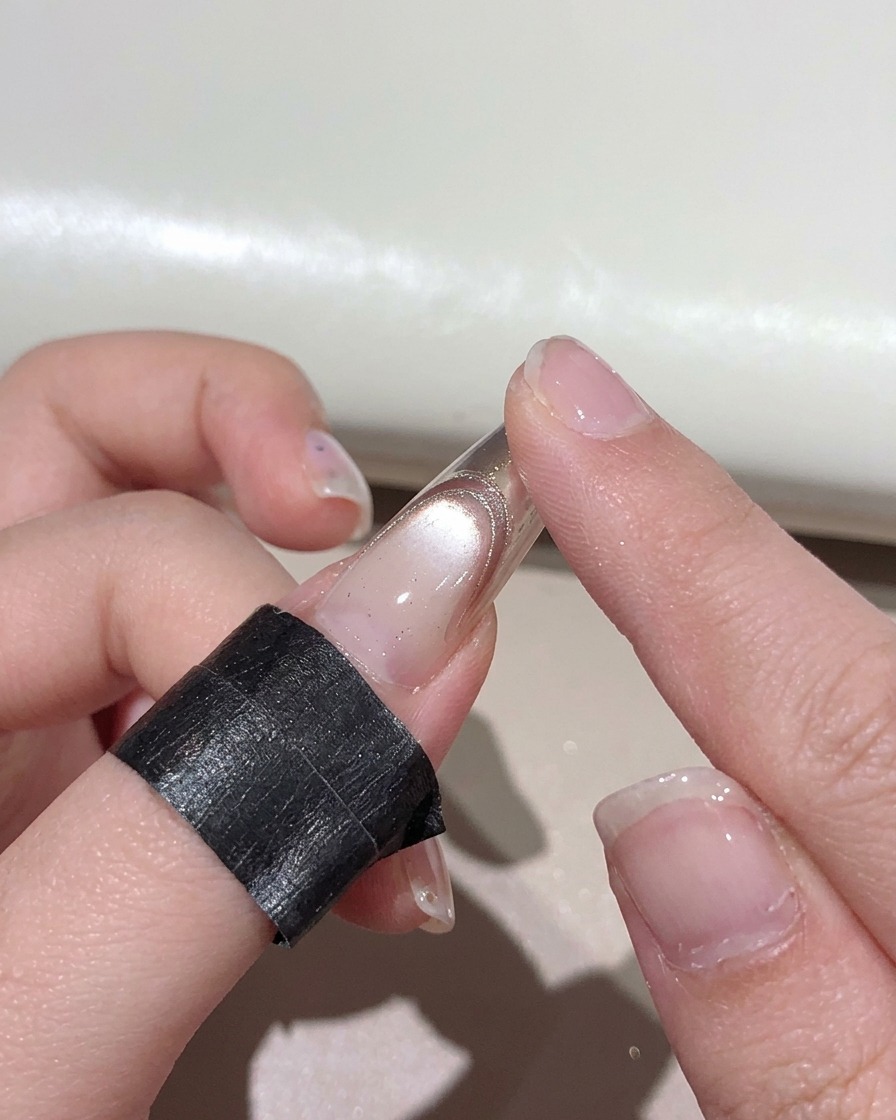 Un doigt frottant de la poudre métallique or rose sur le bout dun ongle manucuré.