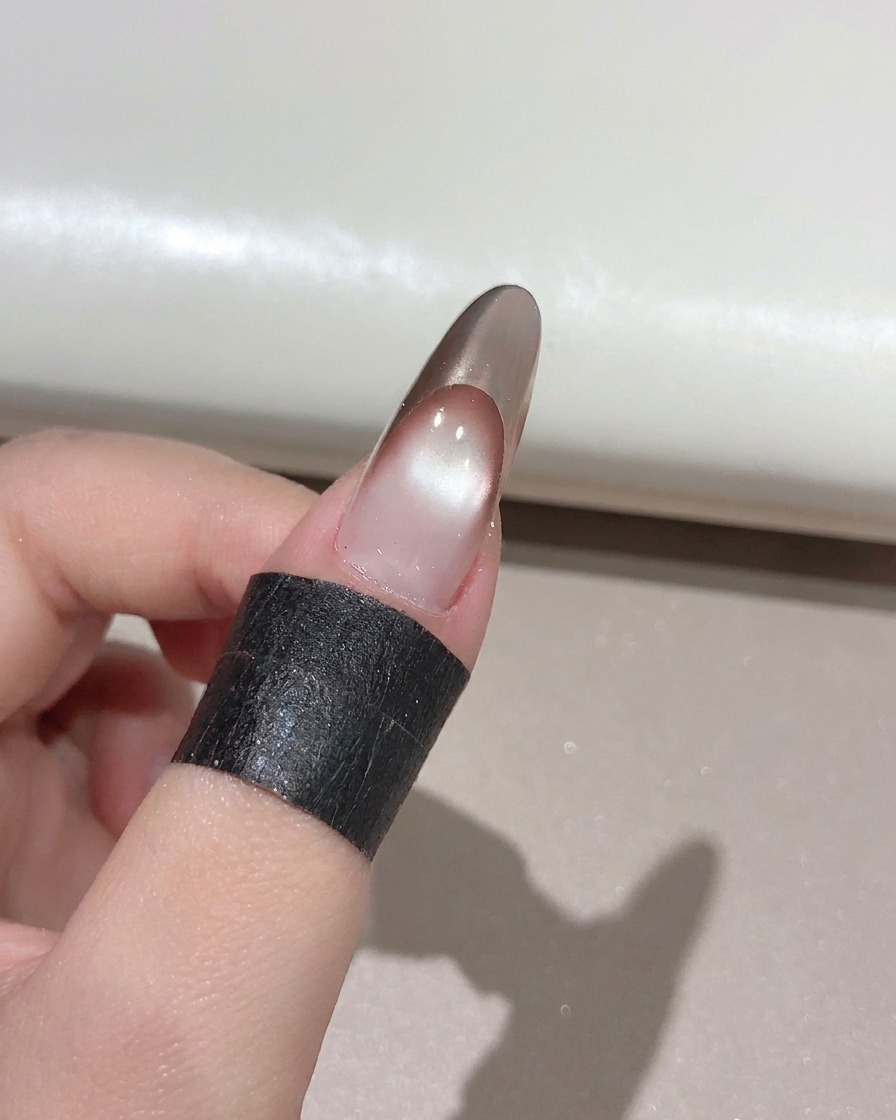 Un pinceau à ongle appliquant un top coat brillant transparent sur une French manucure or rose finie.