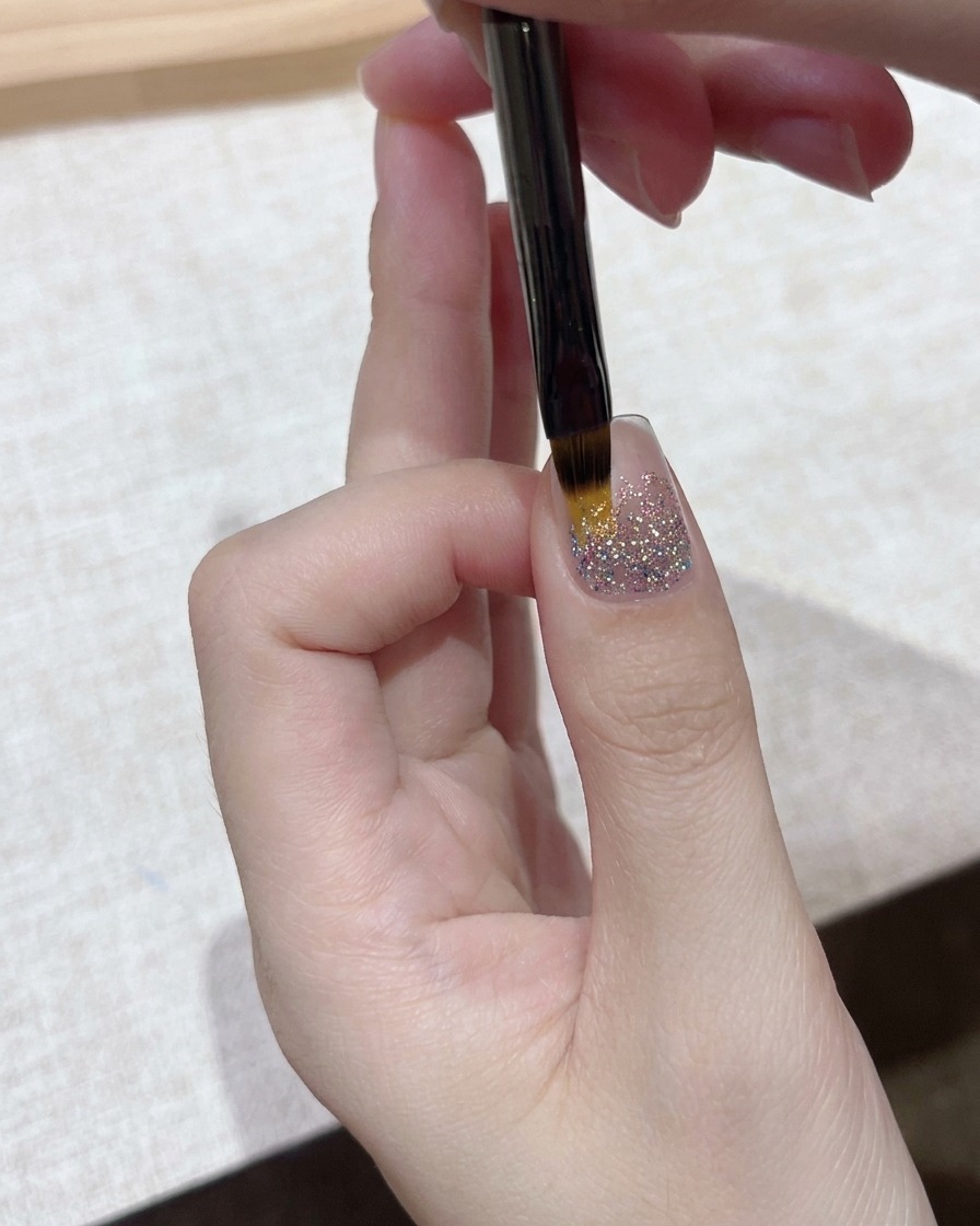 Vue rapprochée dun pinceau de détail appliquant une fine couche de gel transparent sur une base dongle à paillettes scintillantes.