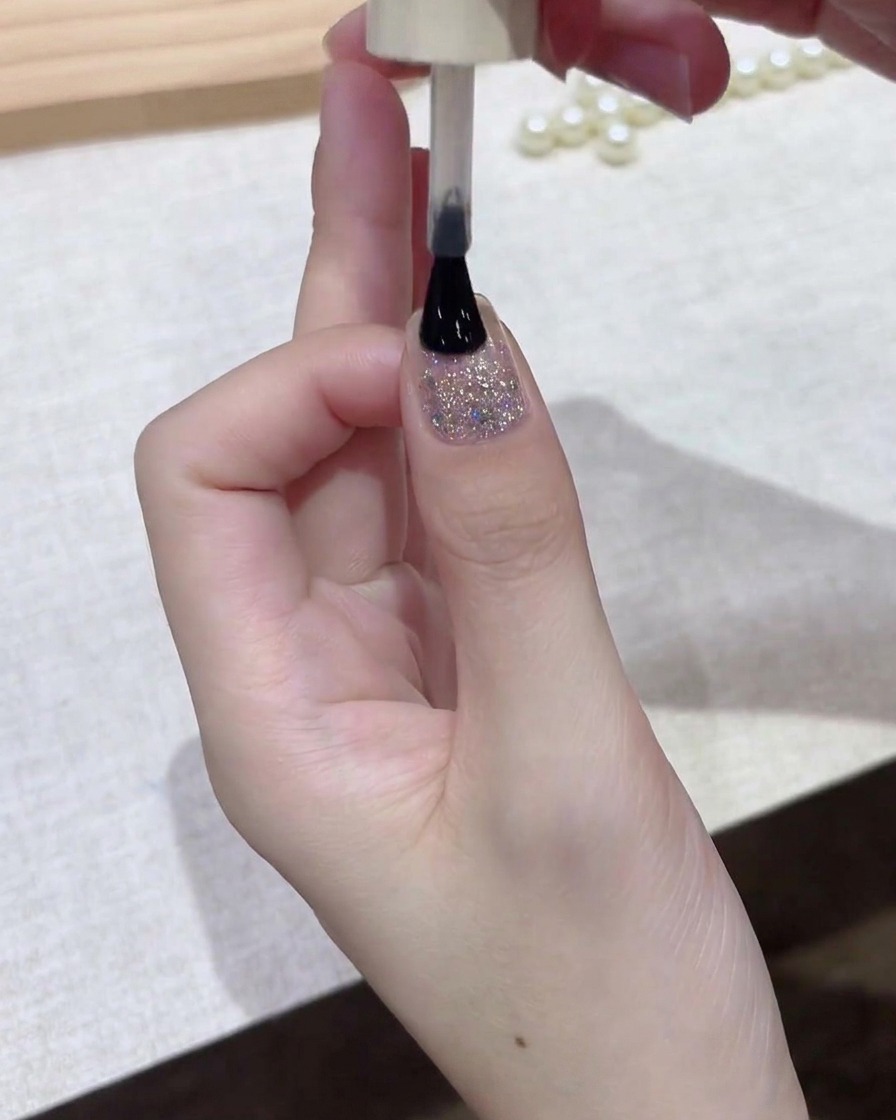 Un pinceau à vernis appliquant une fine couche de gel sombre sur toute la surface de longle.