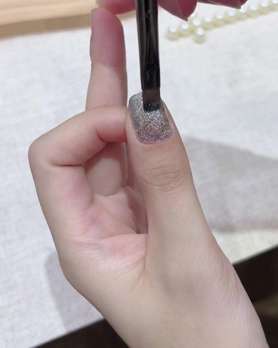 Un pinceau fin lissant uniformément une couche de gel sombre sur la plaque de longle.