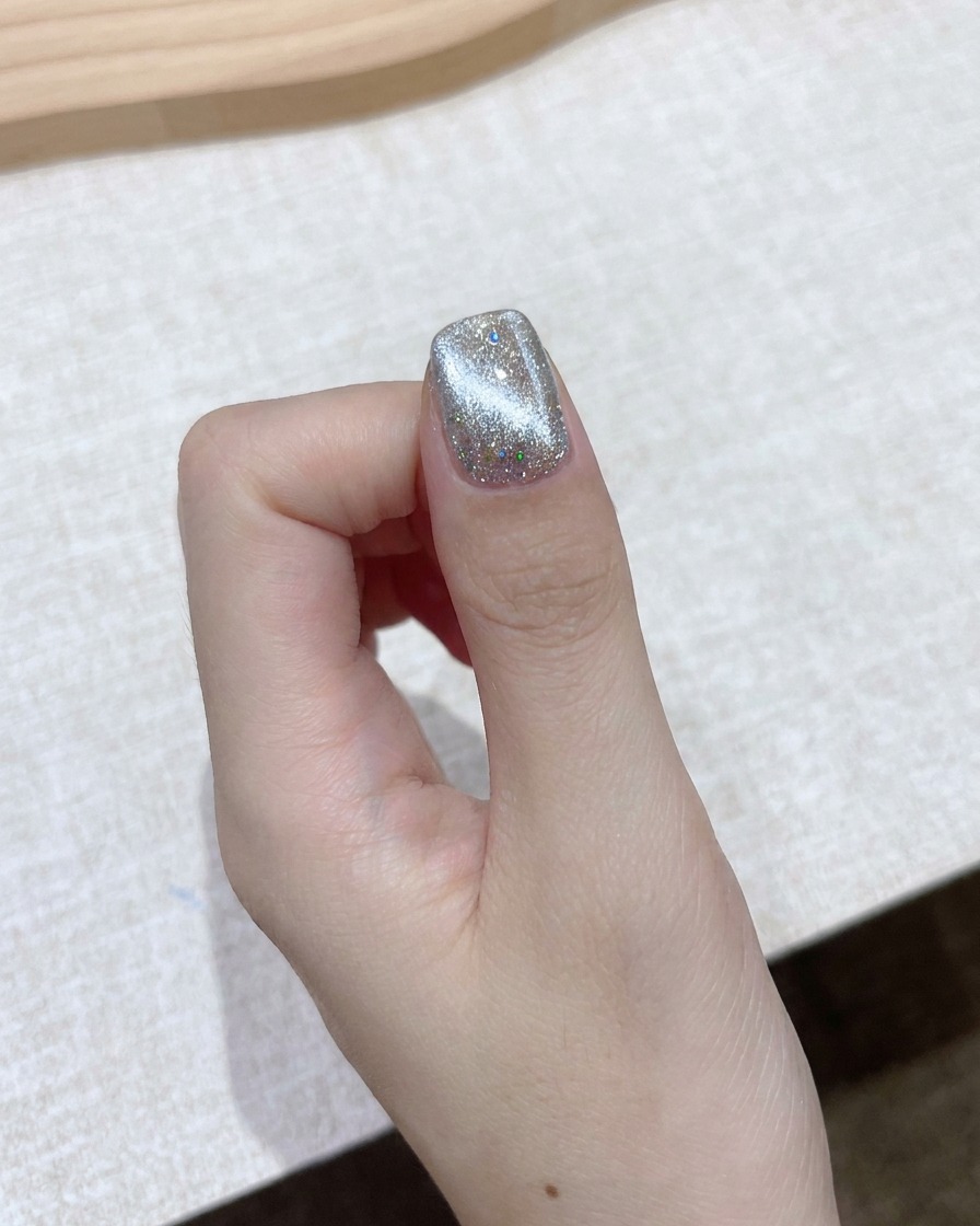 Un aimant bloc rectangulaire tenu près dun ongle en gel œil-de-chat chatoyant pour former un faisceau aurora lumineux.