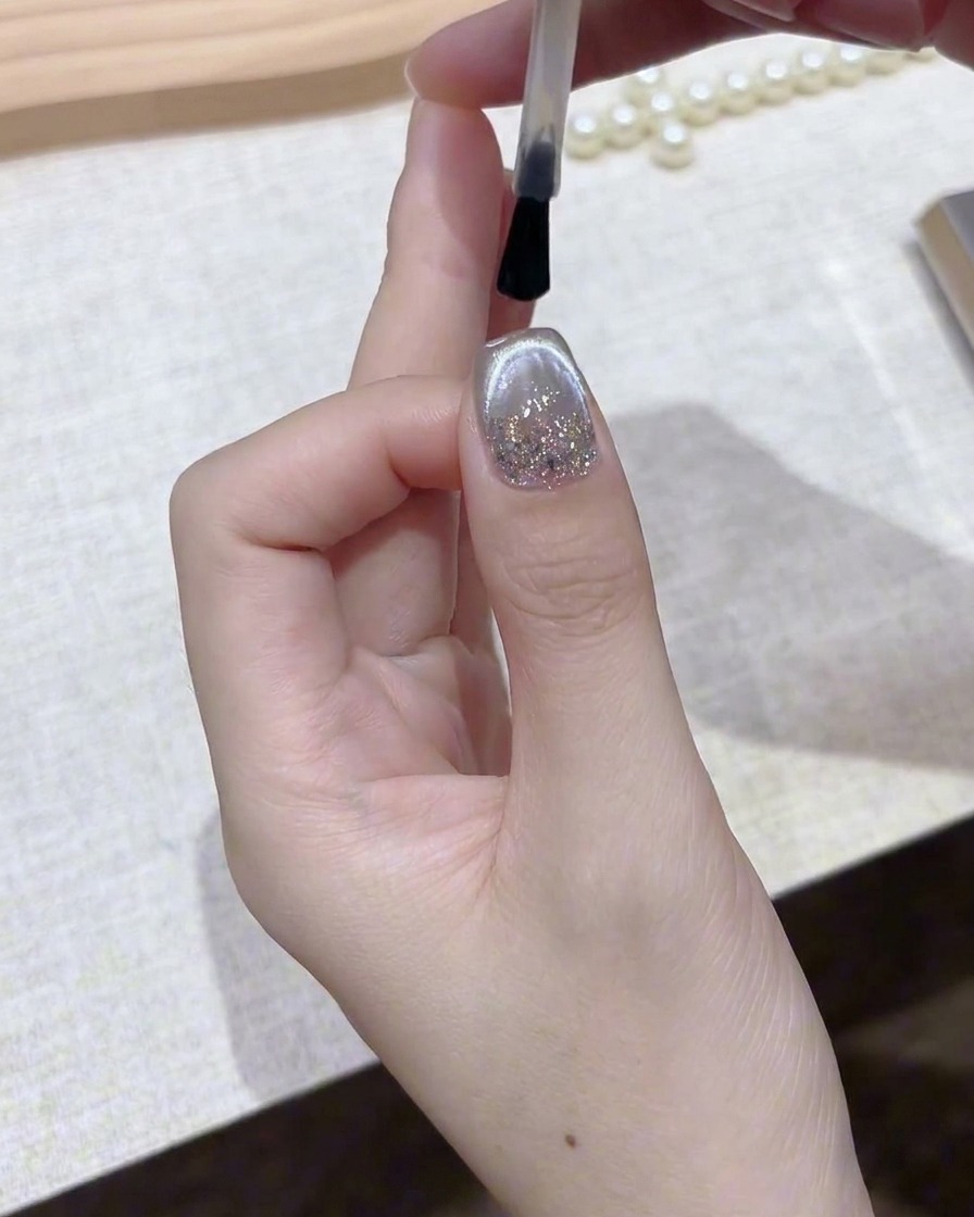 Un pinceau appliquant une couche de finition claire et brillante sur un ongle en gel magnétique argenté fini.
