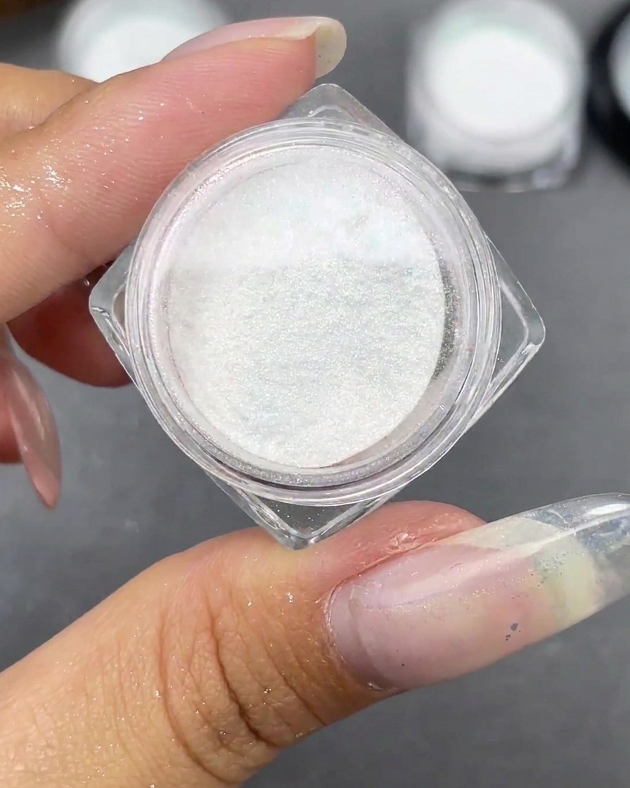 Un petit pot de poudre blanche Moonlight ouvert à côté dune capsule dongle stiletto claire.