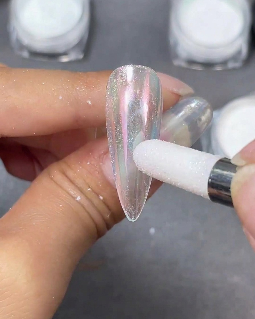Un applicateur en mousse blanc polissant de la poudre nacrée Moonlight sur une capsule dongle stiletto claire, créant un reflet irisé.