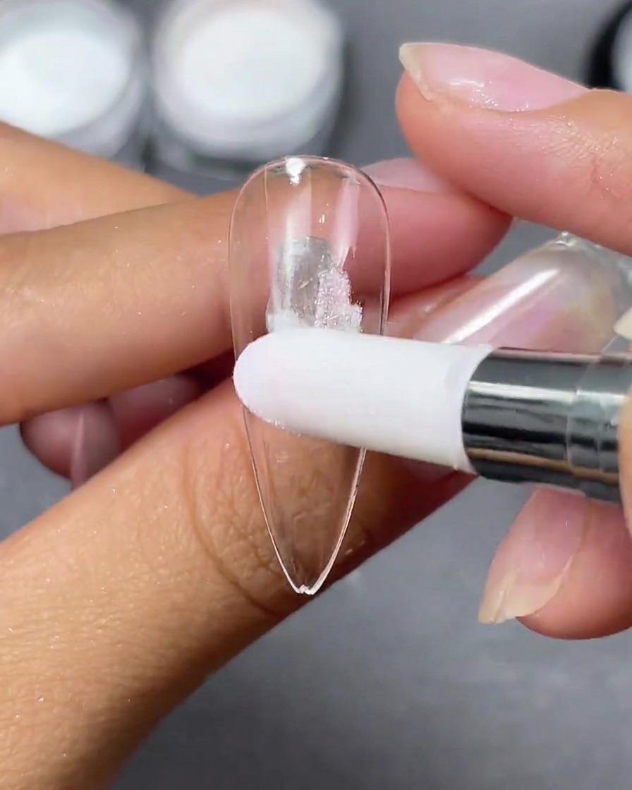 Un applicateur en mousse tamponnant de la poudre blanche Aurora sur une capsule dongle stiletto claire.