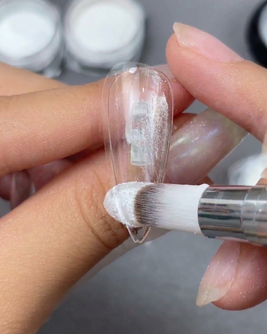 Un applicateur en mousse lustrant de la poudre Aurora sur une capsule dongle claire pour révéler un reflet irisé.