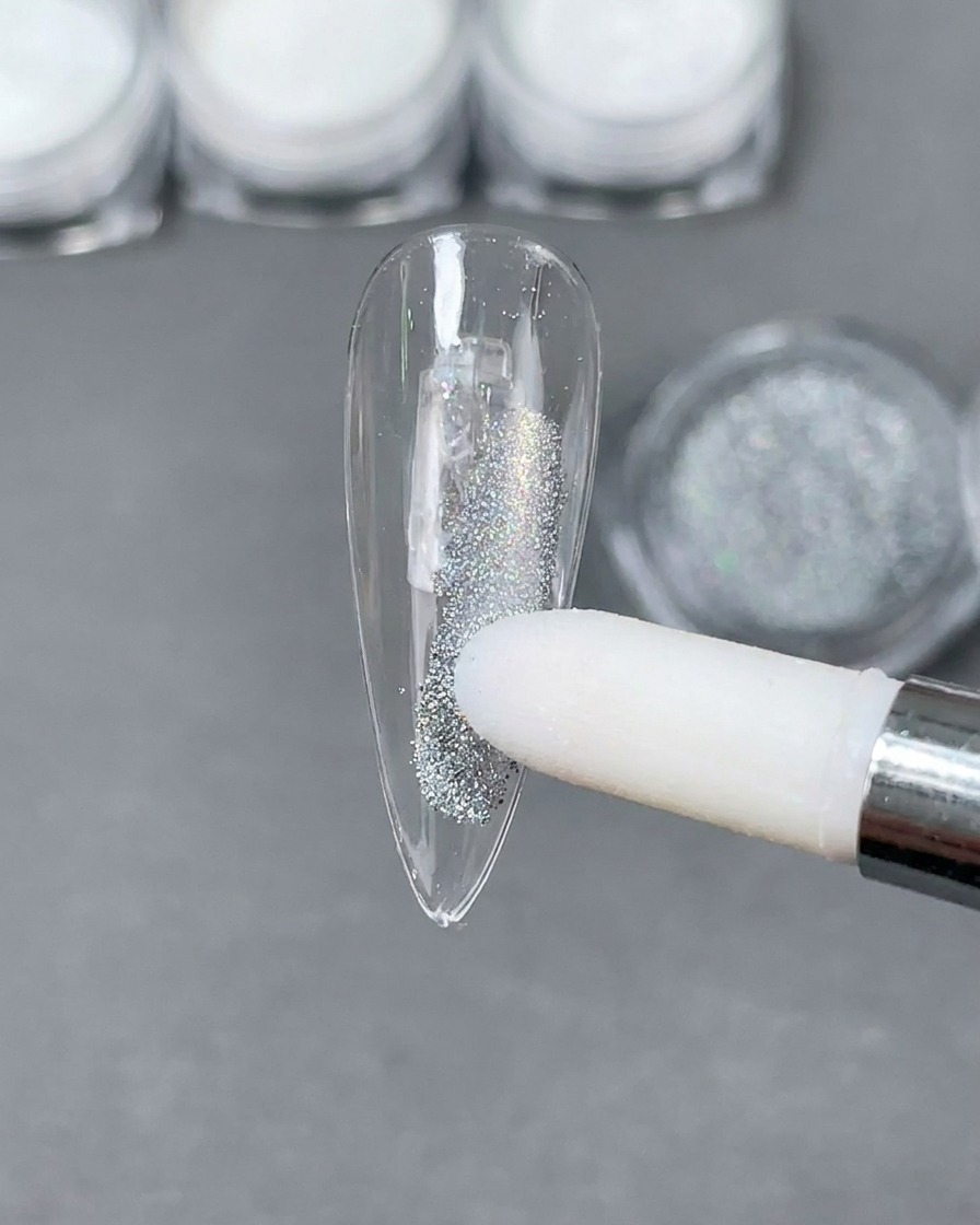 Un applicateur en mousse déposant de la poudre holographique Laser argentée sur une capsule dongle stiletto claire.