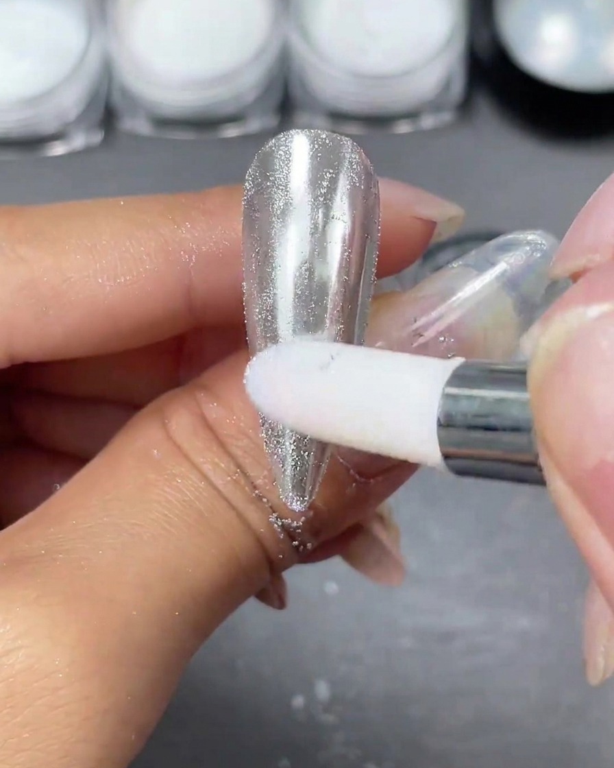 Un applicateur en mousse frottant de la poudre chrome argentée sur une capsule dongle claire jusquà ce quune surface miroir brillante et réfléchissante apparaisse.