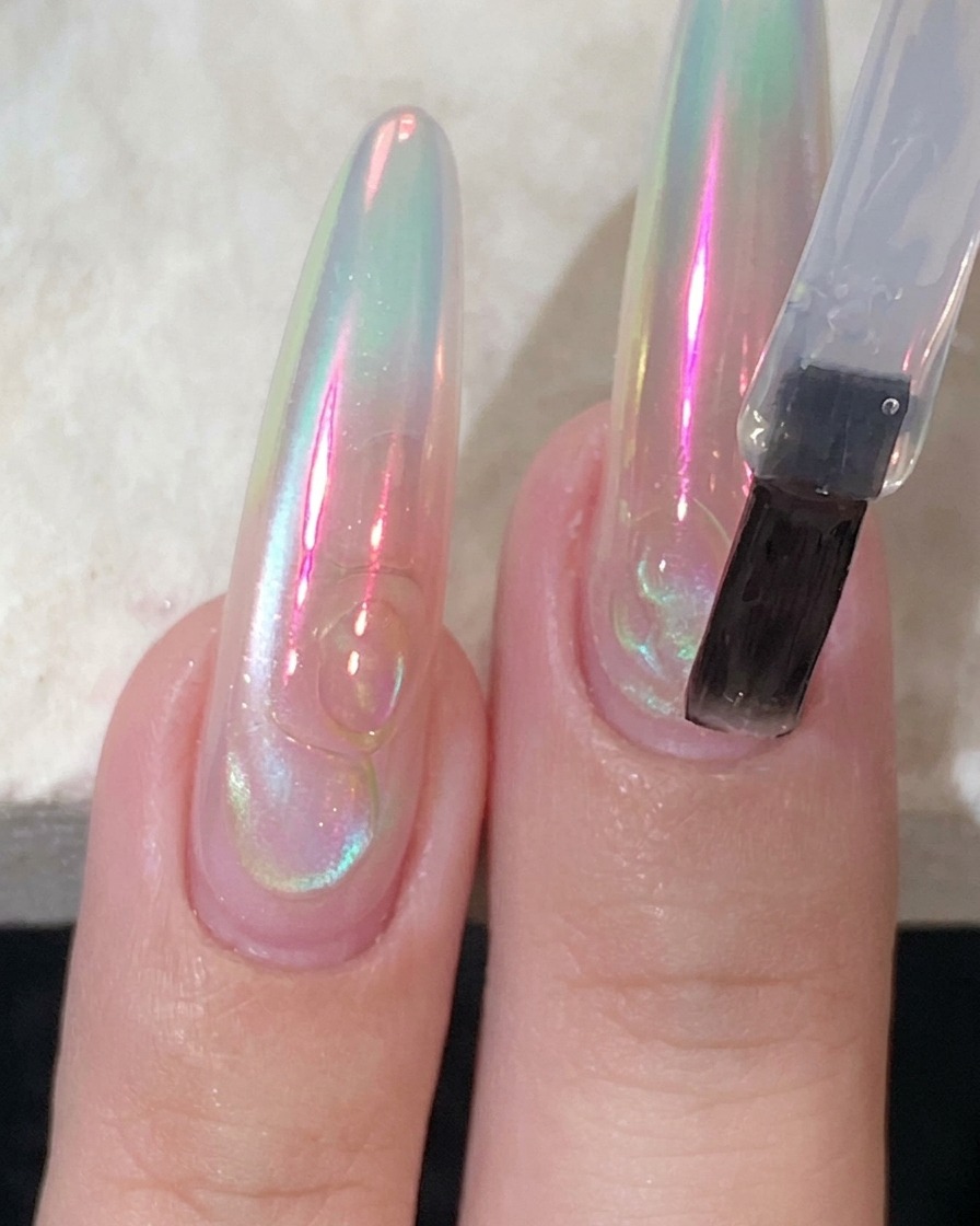Un pinceau à ongles plat appliquant un top coat transparent et brillant sur un ongle long en extension.