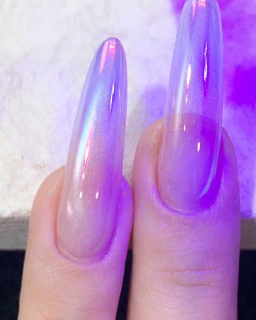 Doigts avec du gel à ongles cat-eye en train de catalyser sous une lampe à ongles UV/LED violette.