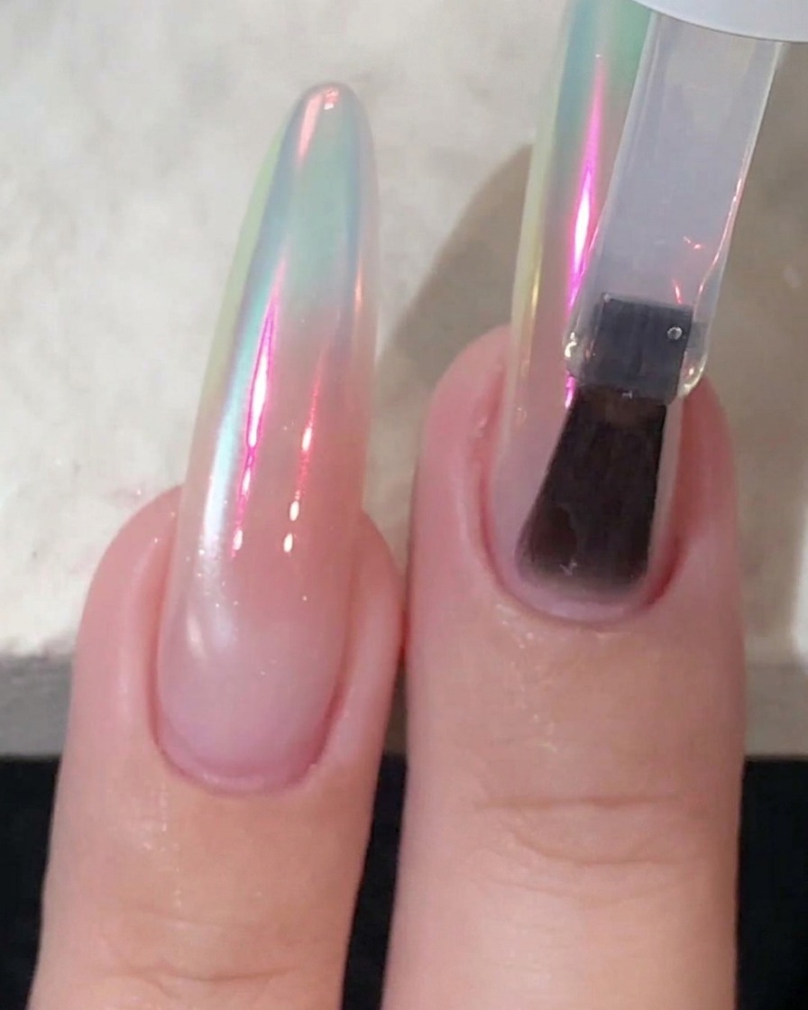 Un applicateur éponge frottant de la poudre chrome sur un ongle brillant jusquà obtenir un reflet aurora.