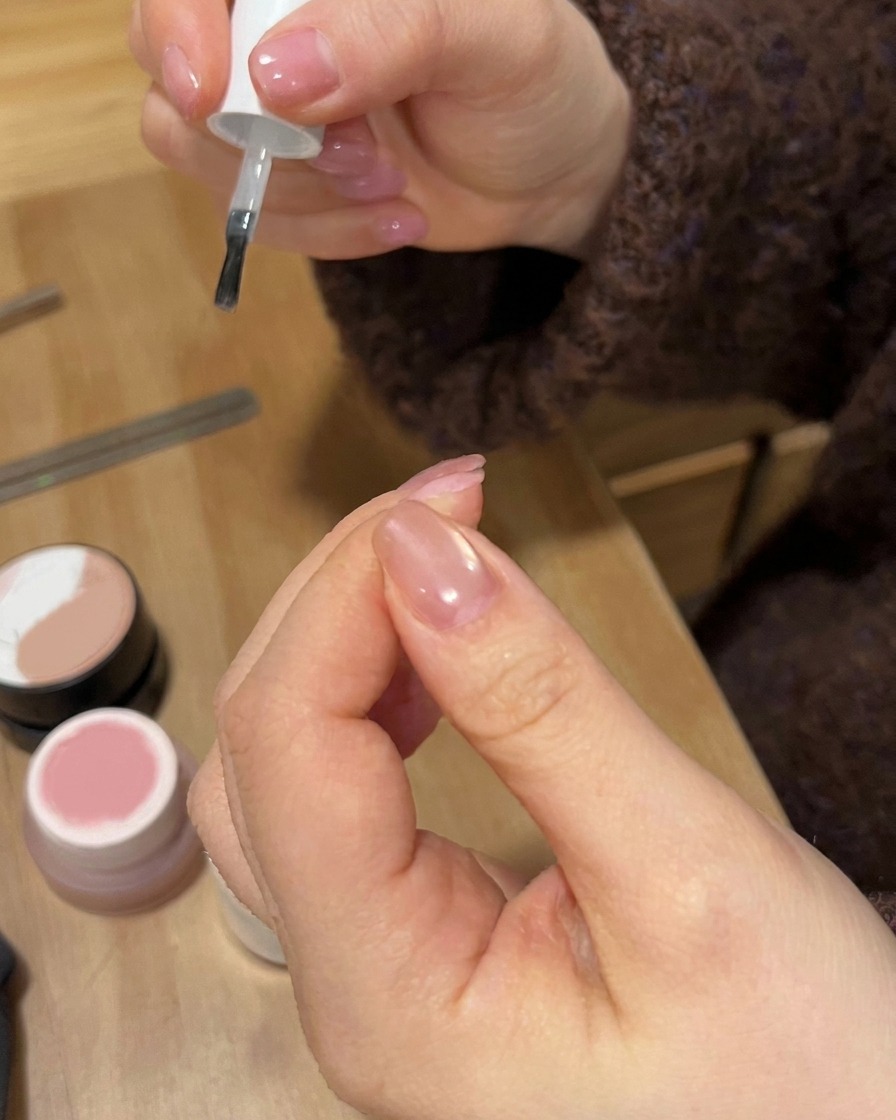 Un pinceau de vernis à ongles appliquant une couche transparente brillante sur un design dongle en dégradé terminé.