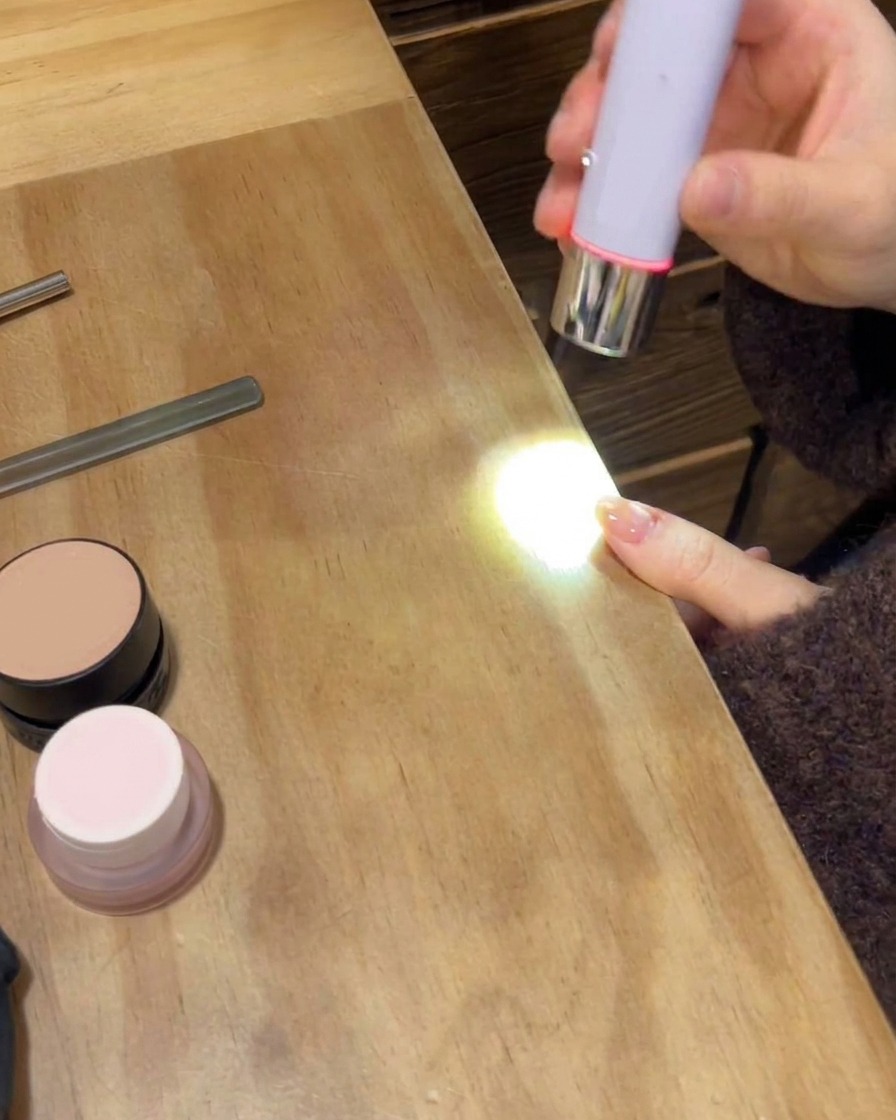 Une lampe UV/LED portable catalysant la couche de finition brillante finale sur une main manucurée.
