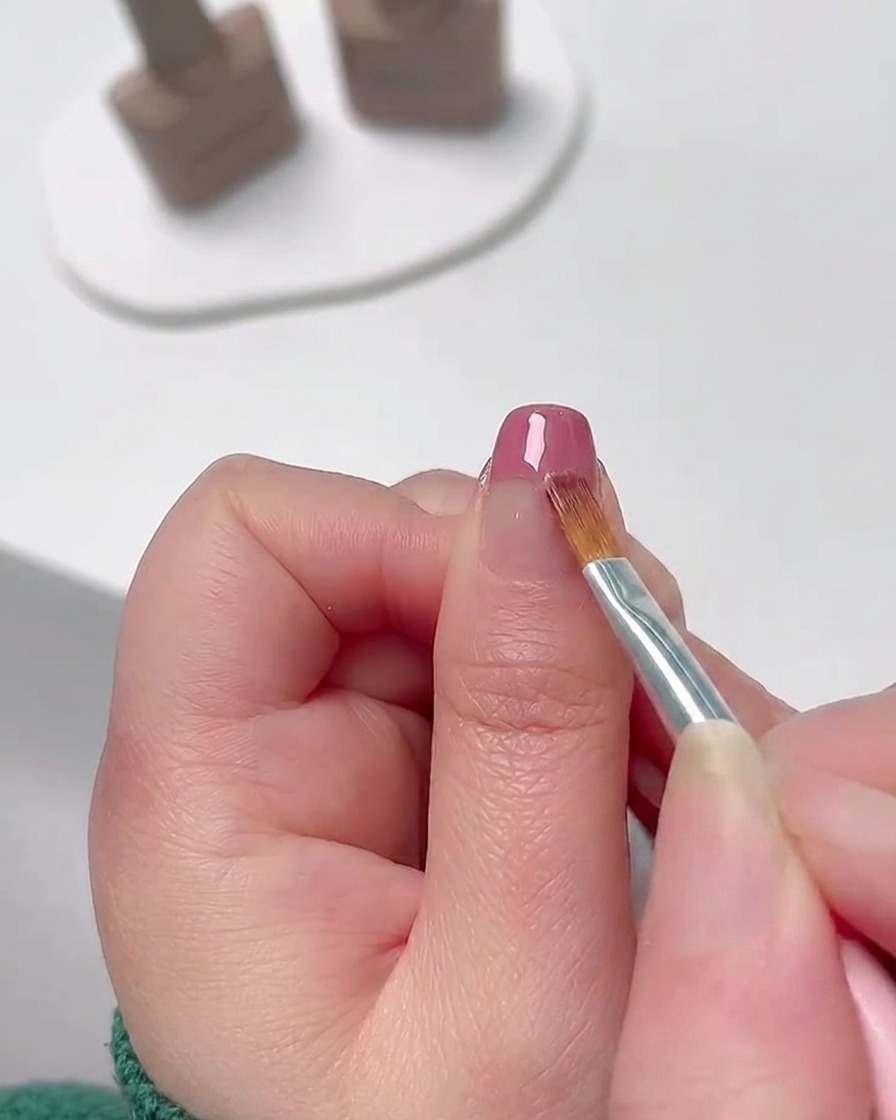 Gros plan dun pinceau de nail art fin estompant du vernis gel rose depuis le bout de longle pour créer un dégradé de couleur doux.