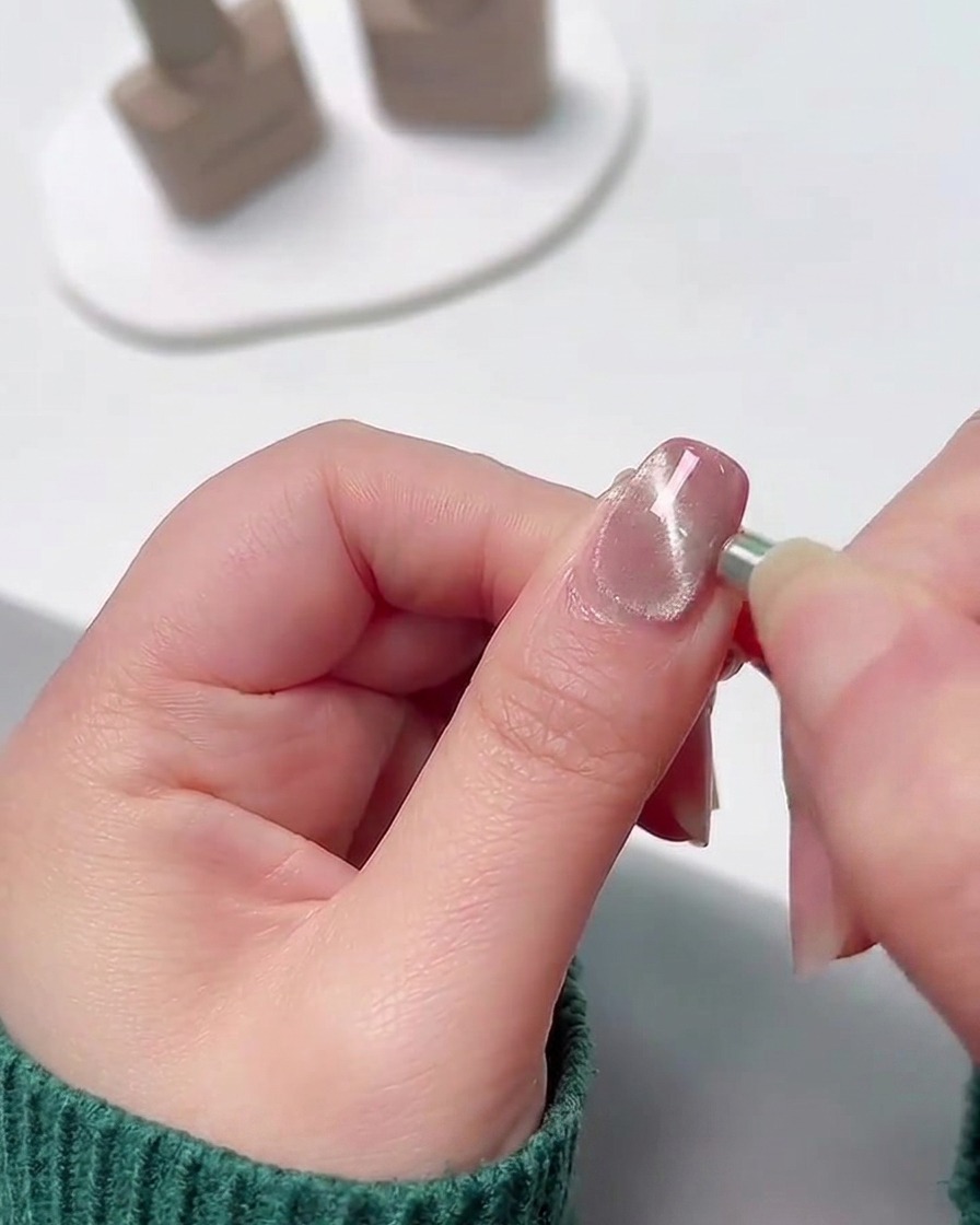 Gros plan dun petit aimant cylindrique tenu contre le bord latéral dun ongle en gel humide et scintillant pour attirer les particules métalliques en une ligne concentrée.