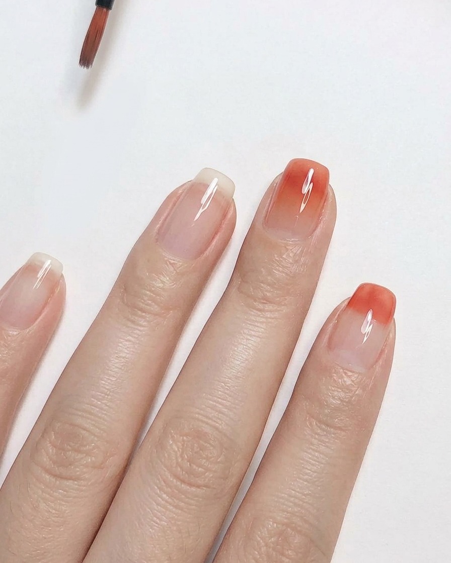 Un pinceau de détail estompant un vernis gel rose pêche vers le haut sur un ongle transparent pour créer un effet dégradé ombré.