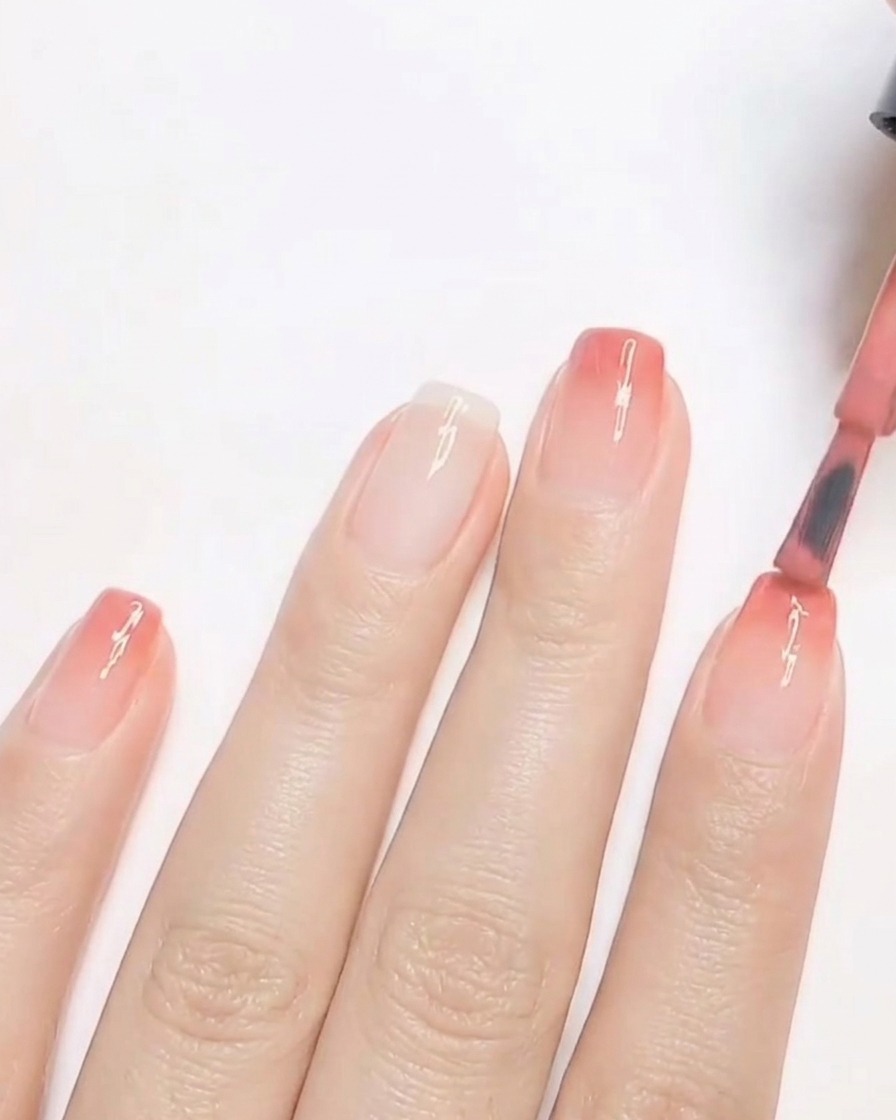 Un pinceau appliquant une deuxième couche de vernis gel pêche chaud sur le bout de longle pour intensifier le dégradé.