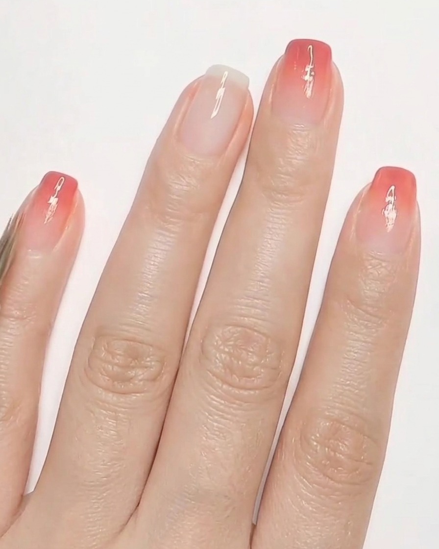 Un pinceau ultra fin dessinant de petits cœurs rouges sur un ongle avec une base blanc laiteux.