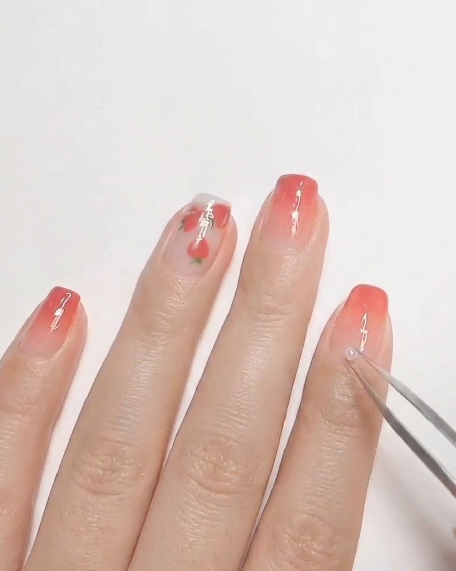 Une pince à épiler plaçant une petite perle blanche sur du gel non catalysé sur un ongle.