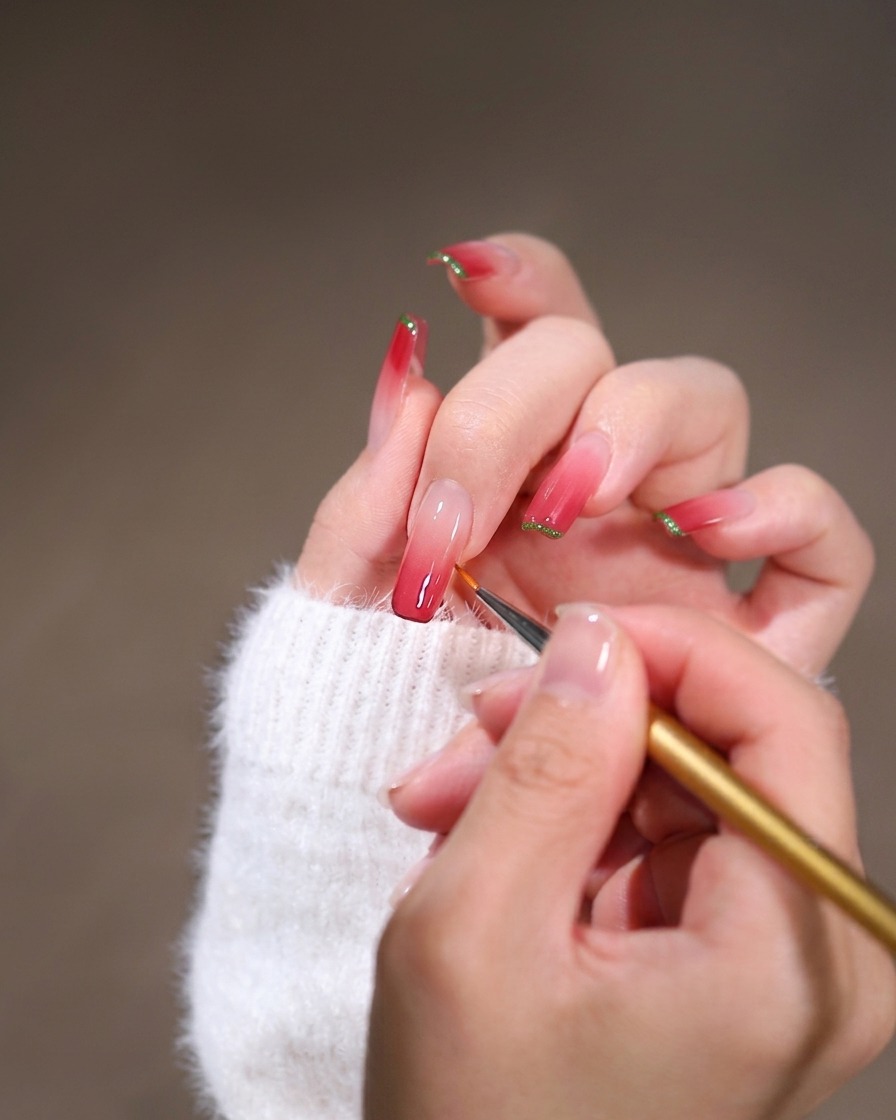 Gros plan dun pinceau liner fin estompant du gel rose le long de la cuticule sur un long ongle carré.