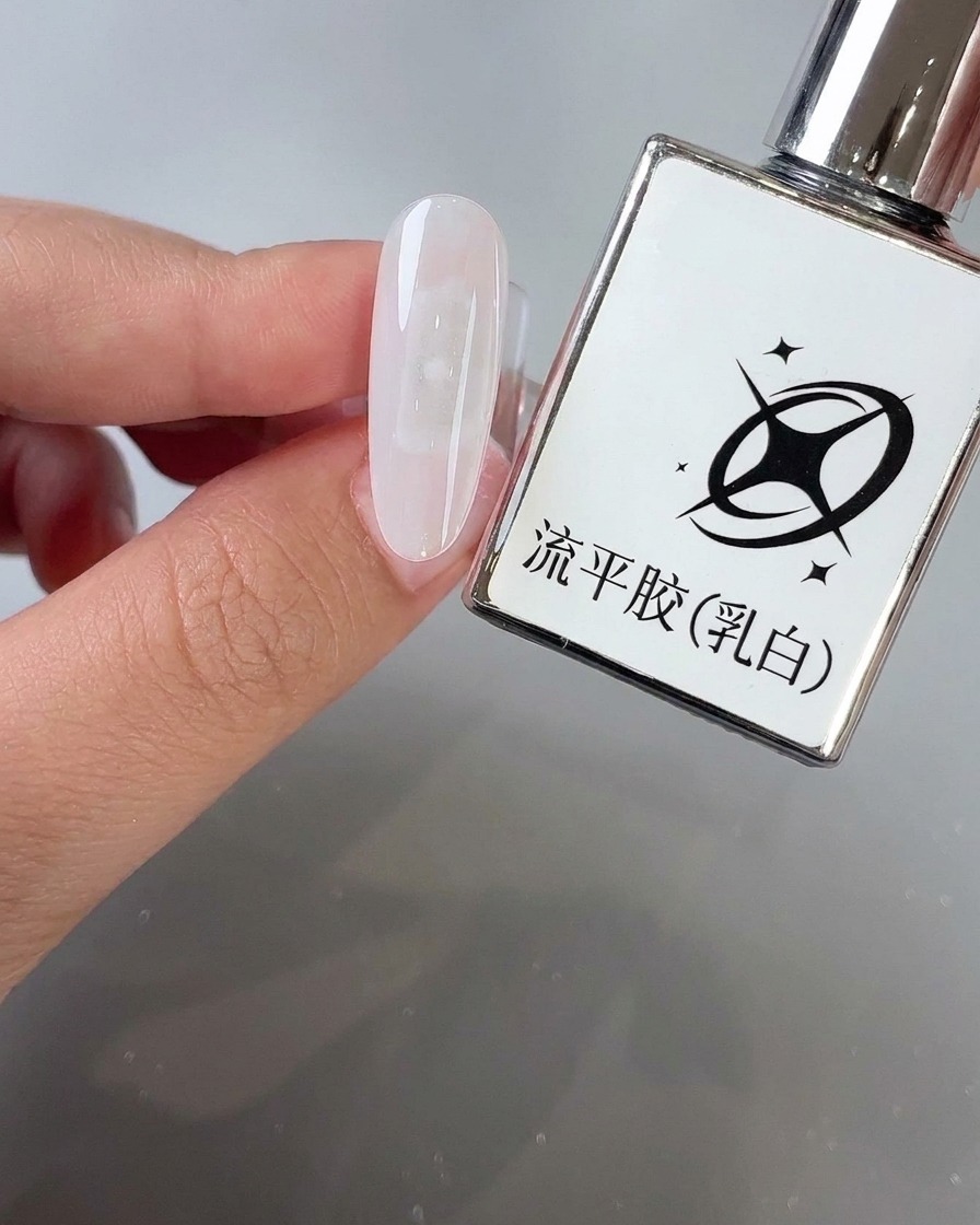 Un pinceau appliquant du gel autonivelant blanc laiteux sur la surface dun onglet en amande à côté de son flacon de produit.