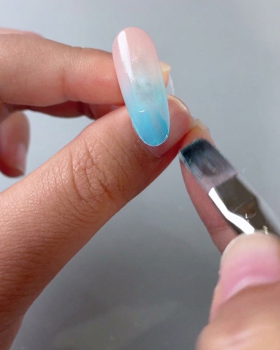 Un pinceau appliquant une seconde couche de gel vitrail bleu sur la moitié avant de la pointe de longle.