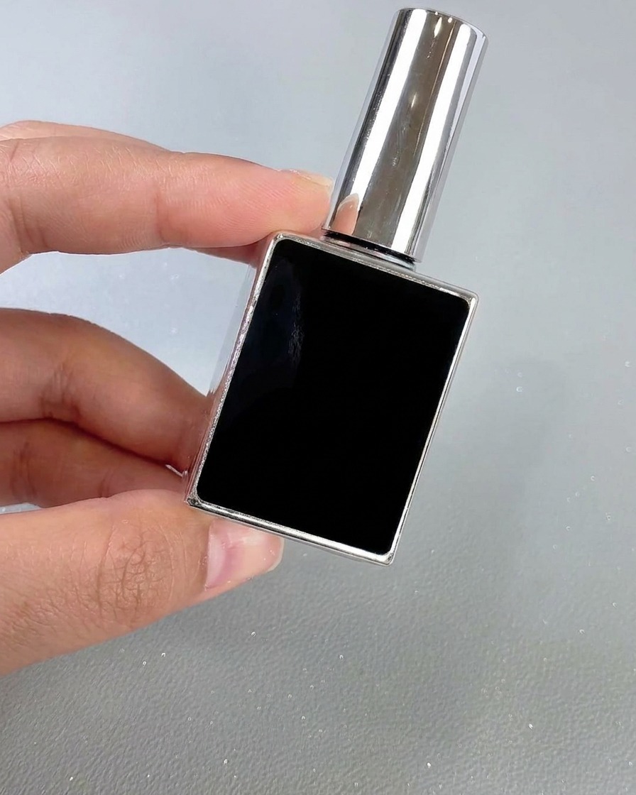 Un flacon carré noir et argenté de top coat pour ongles tenu à la main sur un fond neutre.