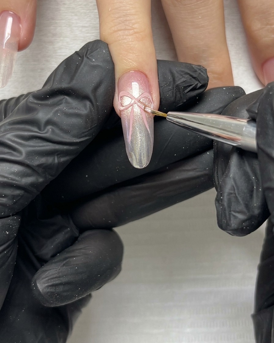 Gros plan dun pinceau fin affinant les bords délicats et les pans dun nœud en ruban rose 3D sur un ongle manucuré.