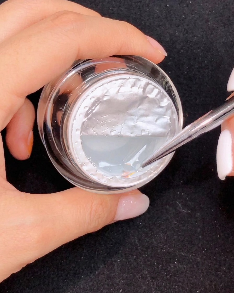 Un pinceau fin étirant une longue forme de goutte en gel transparent sur un ongle rose dégradé.