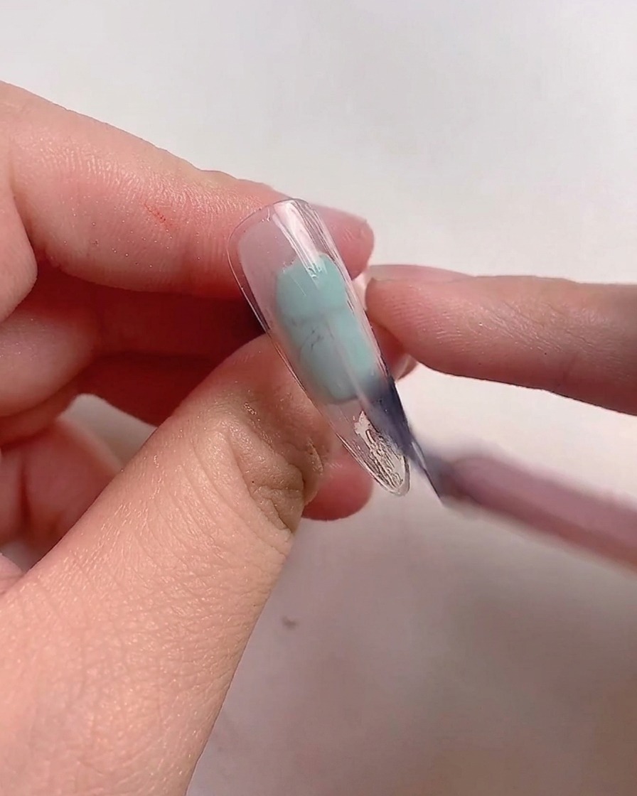 Un pinceau appliquant du vernis gel rose mauve sur une capsule dongle transparente.