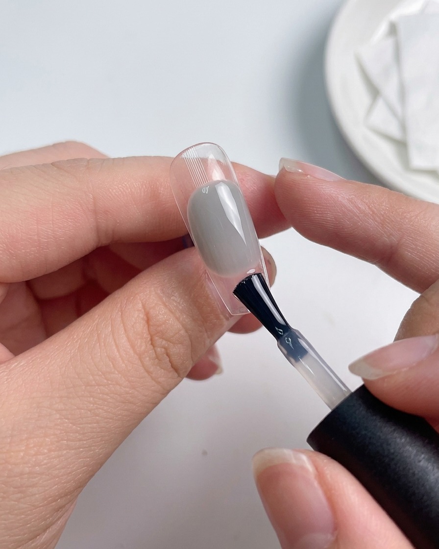 Un pinceau appliquant une couche de finition sur un ongle coloré.