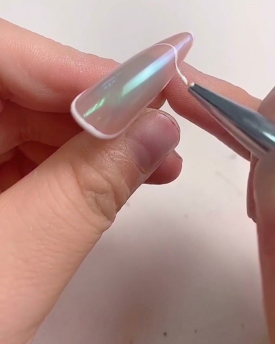 Un pinceau fin appliquant une ligne de gel blanc sur le bord dun ongle en forme damande pour créer une french manucure.