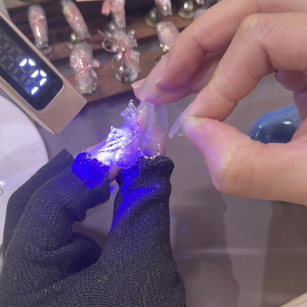 Une mini lampe UV projetant une lumière violette sur une nouvelle aile de papillon en gel rose 3D modelée sur un ongle.