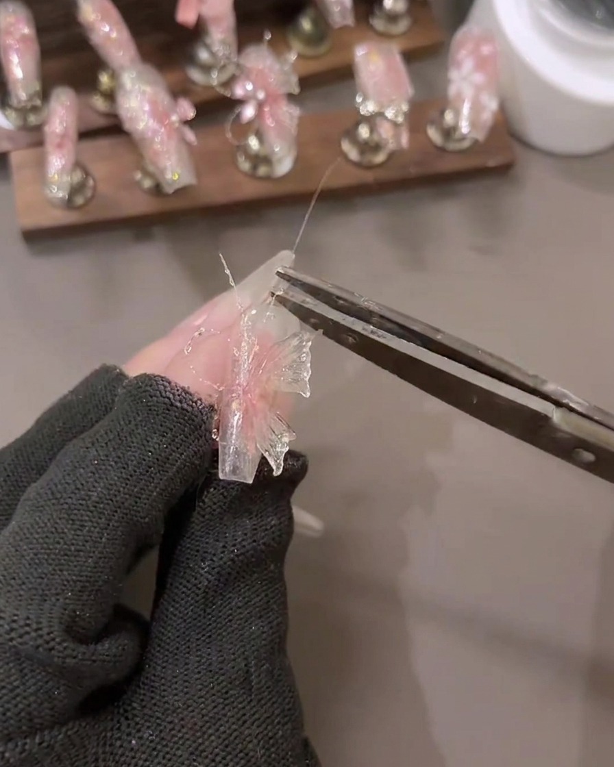 Gros plan dune main appliquant des détails de gel à paillettes diamant brisé sur un design de nail art 3D avec des outils à proximité.