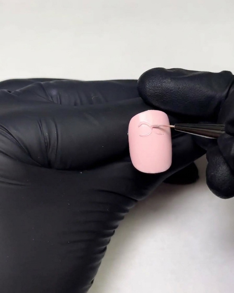 Mains gantées dessinant la deuxième boucle dun nœud en gel 3D sur un ongle à laide dun pinceau liner fin.