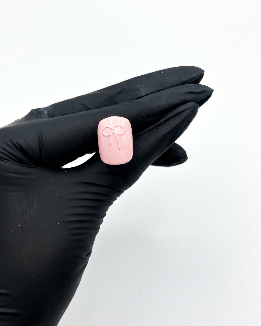 Une main gantée tenant un faux ongle rose sous une lampe UV pour catalyser le motif de nœud 3D.
