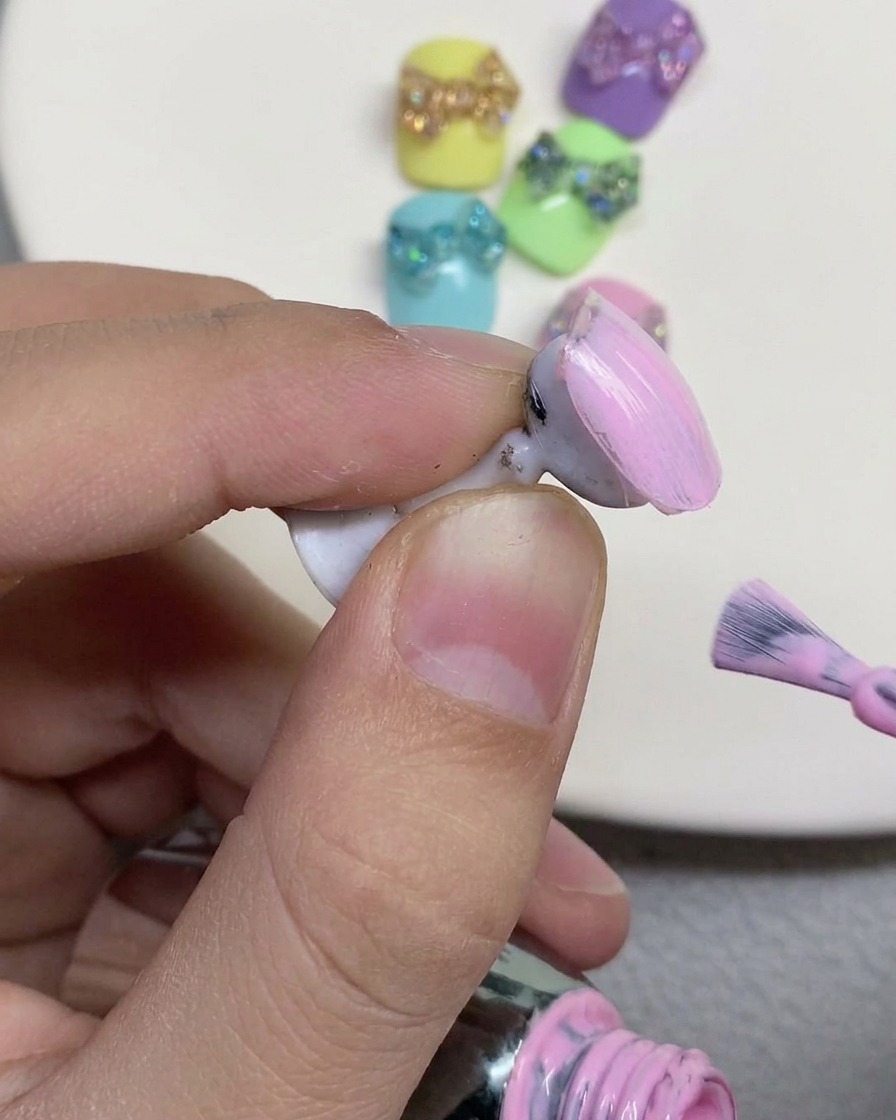 Un pinceau à ongles appliquant un vernis gel rose pastel doux sur la surface dun faux ongle posé sur un support.