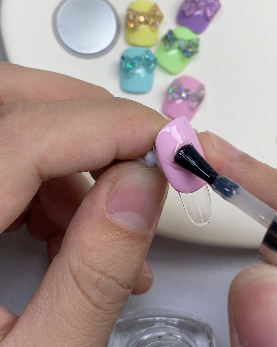 Un pinceau à ongles noir appliquant du gel de renforcement transparent sur un ongle vernis en rose.