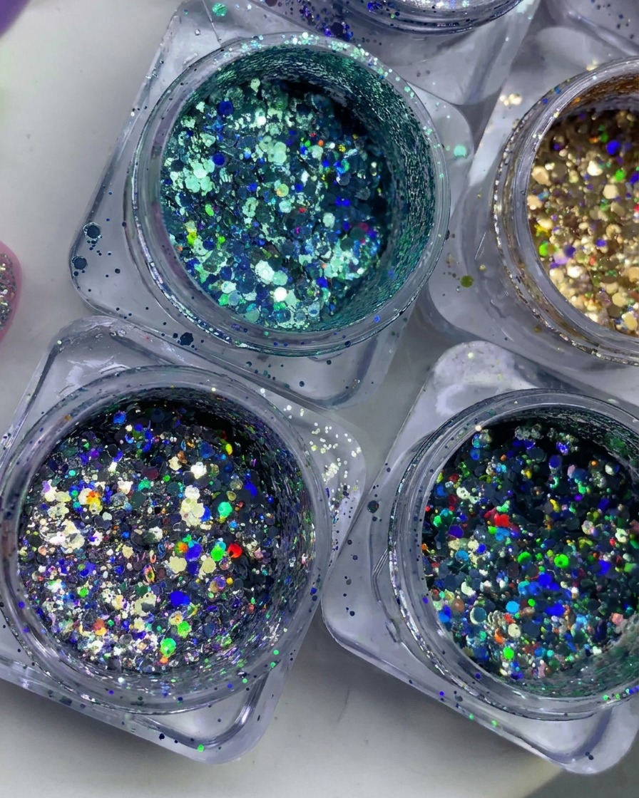 Vue de dessus de plusieurs petits pots remplis de flocons de paillettes colorées, holographiques et métalliques.